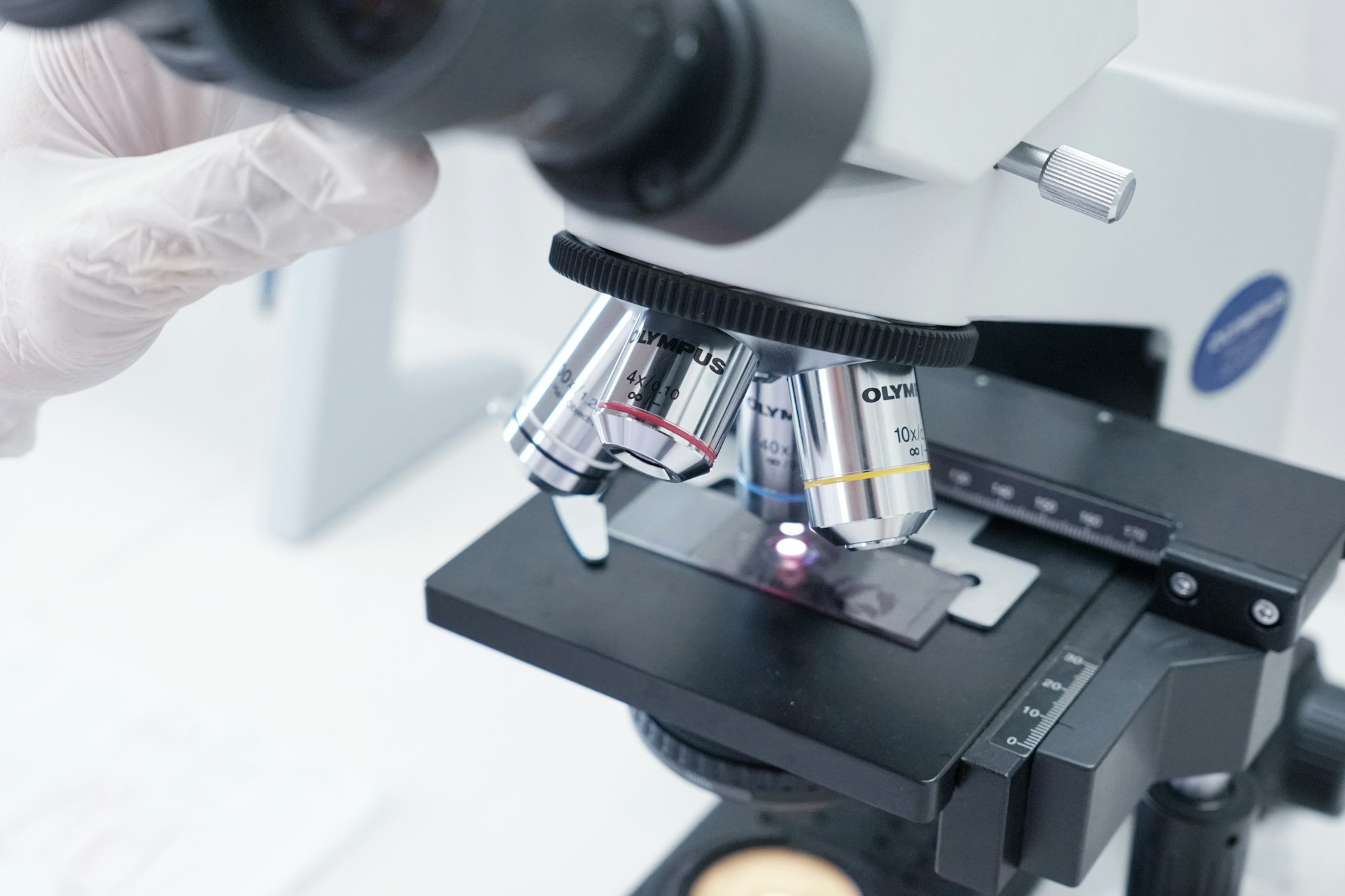 A person in white gloves is looking through a microscope